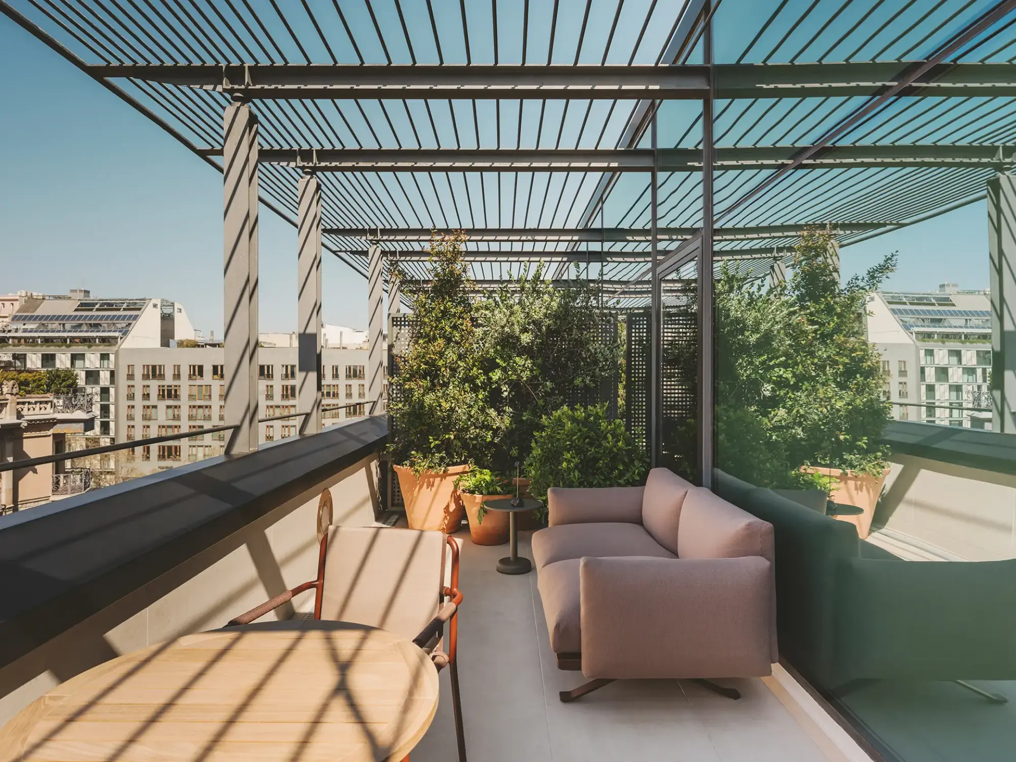 Se ve una terraza con sofá, mesa y plantas en macetas junto a barandillas de vidrio.