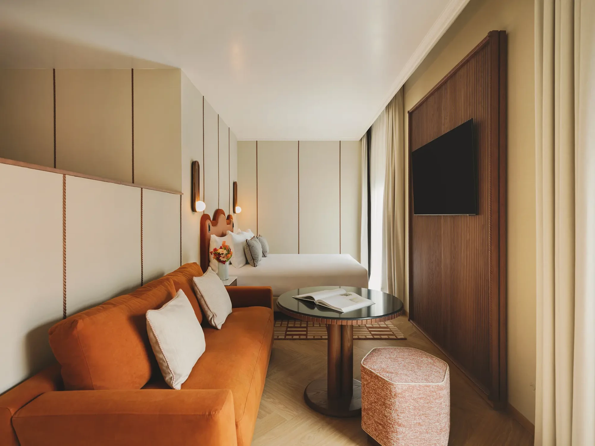 Se ve una sala de estar con sofá, mesa auxiliar, TV y cortinas junto a una cama.