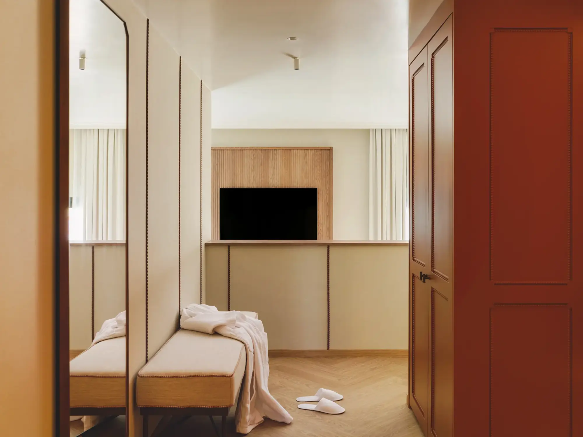 Se ve una cama con ropa de cama blanca, un televisor y una puerta roja en una habitación interior.