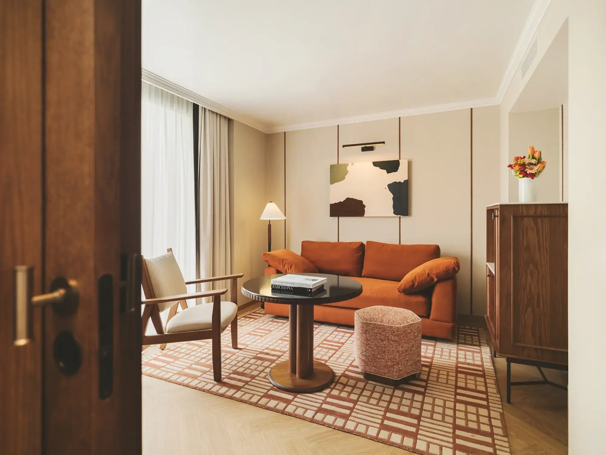 Se ve una sala de estar con sofá naranja, mesa auxiliar, sillón, lámpara y una pared con cuadro.