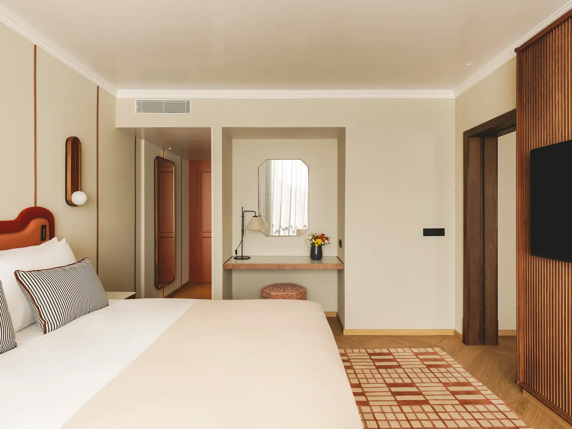Se ve una cama doble, una zona de estar y un tocador con espejo en una suite.