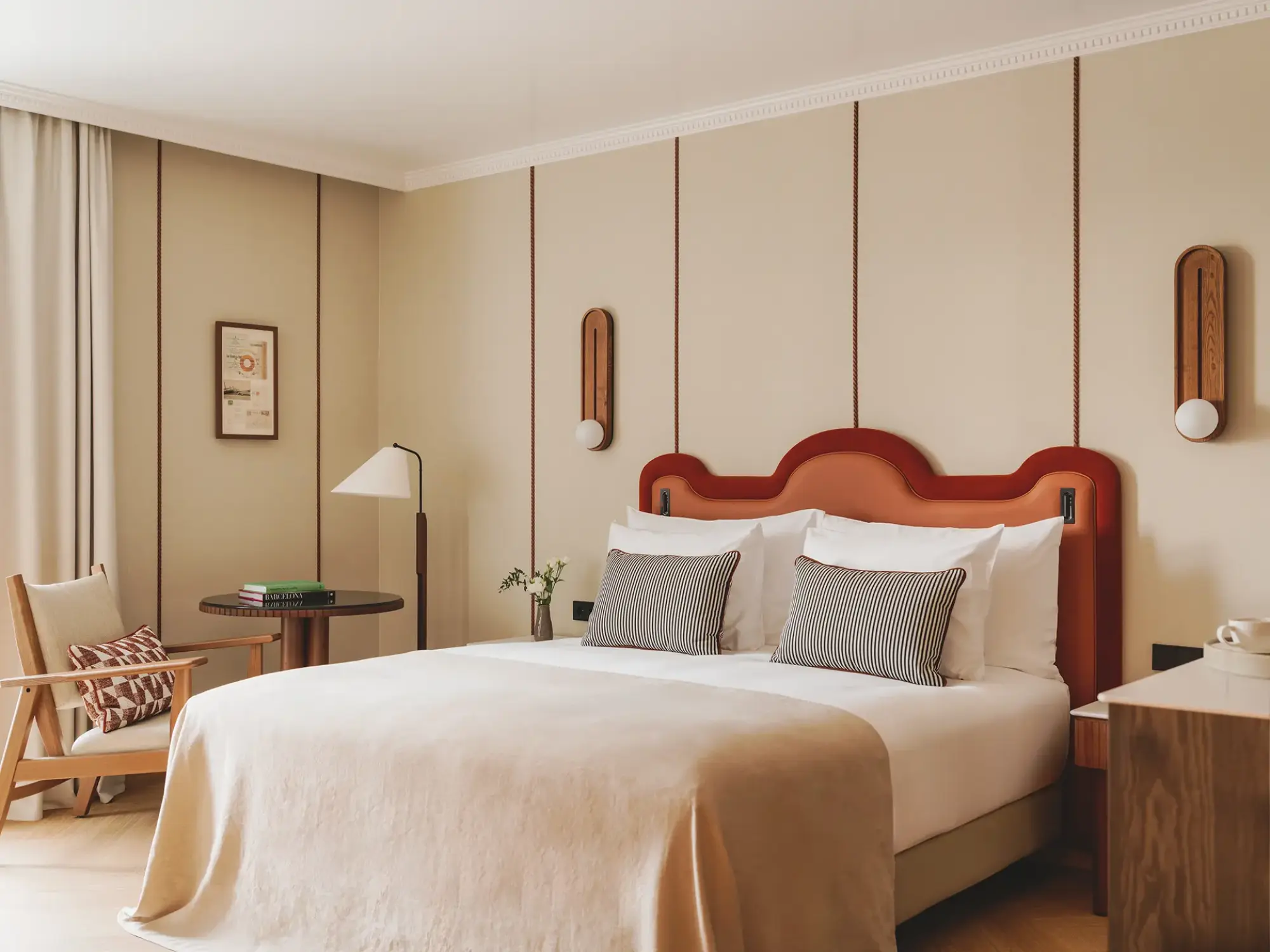 Se ve una cama doble con ropa de cama clara, mesitas laterales y una silla junto a una ventana en la habitación.