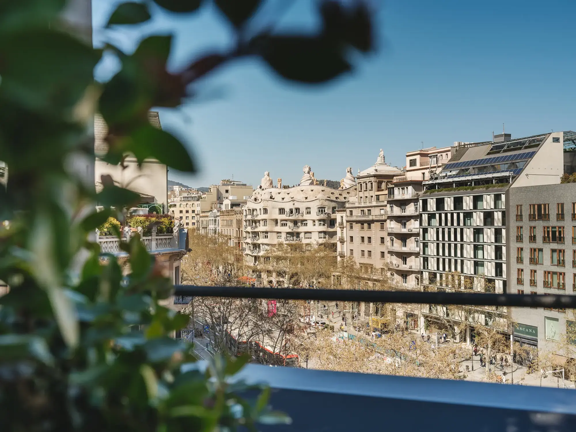 Se ve una terraza con barandilla y edificios en el fondo bajo un cielo despejado.