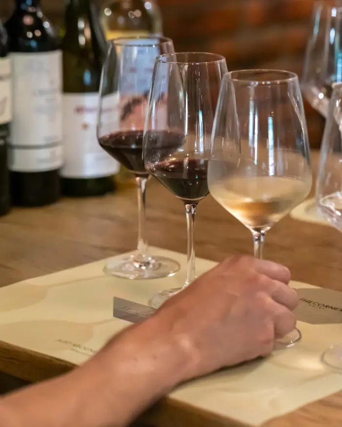 Varias copas de vino y agua se ven sobre una mesa con servilletas y botellas al fondo.