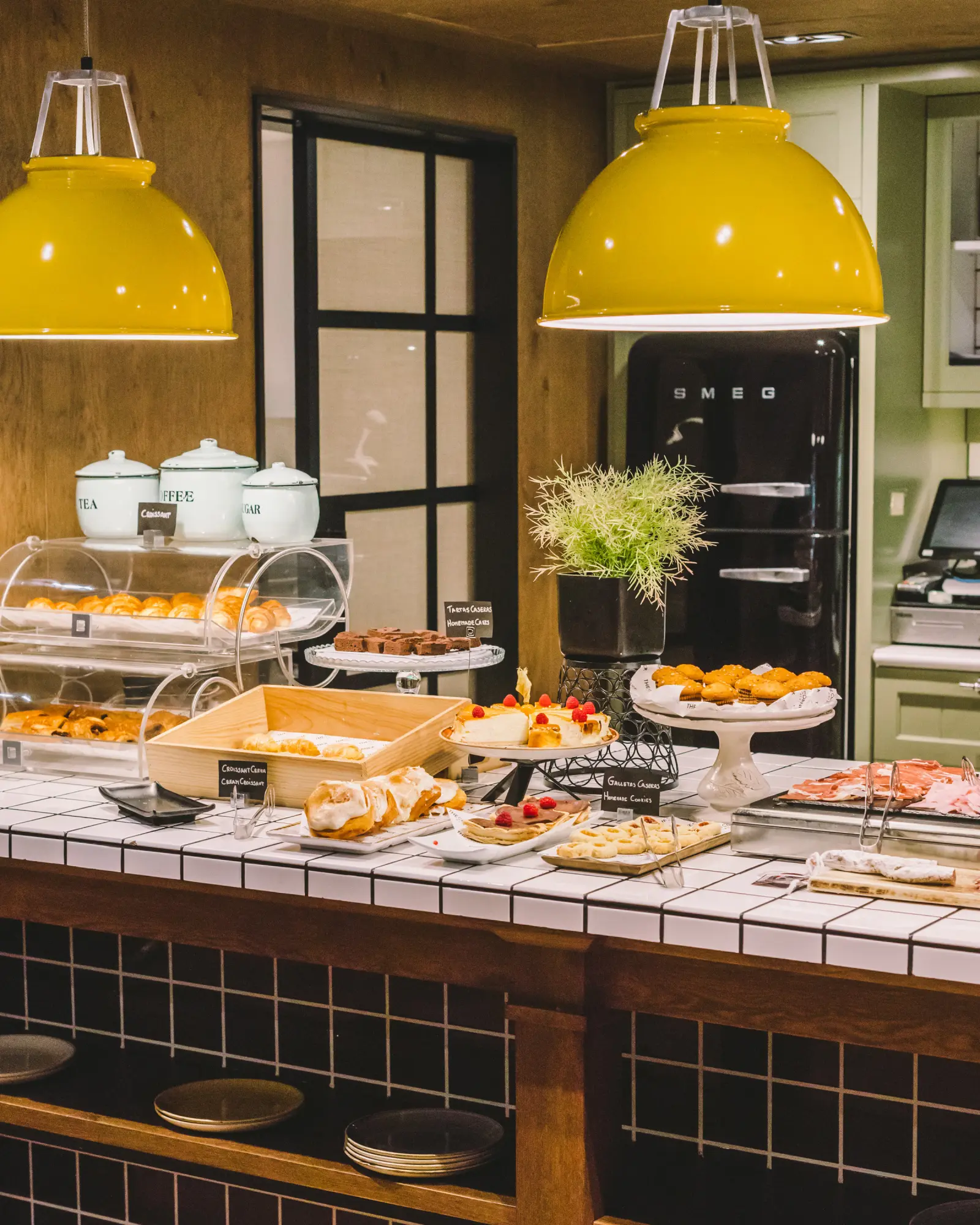 Se ve una mesa con platos y alimentos en un área de desayuno con vitrinas y lámparas colgantes.