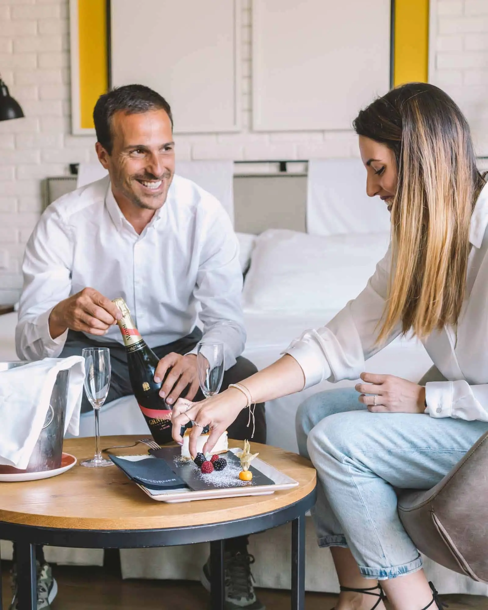 Dos personas brindan junto a la mesa auxiliar de una habitación de hotel.