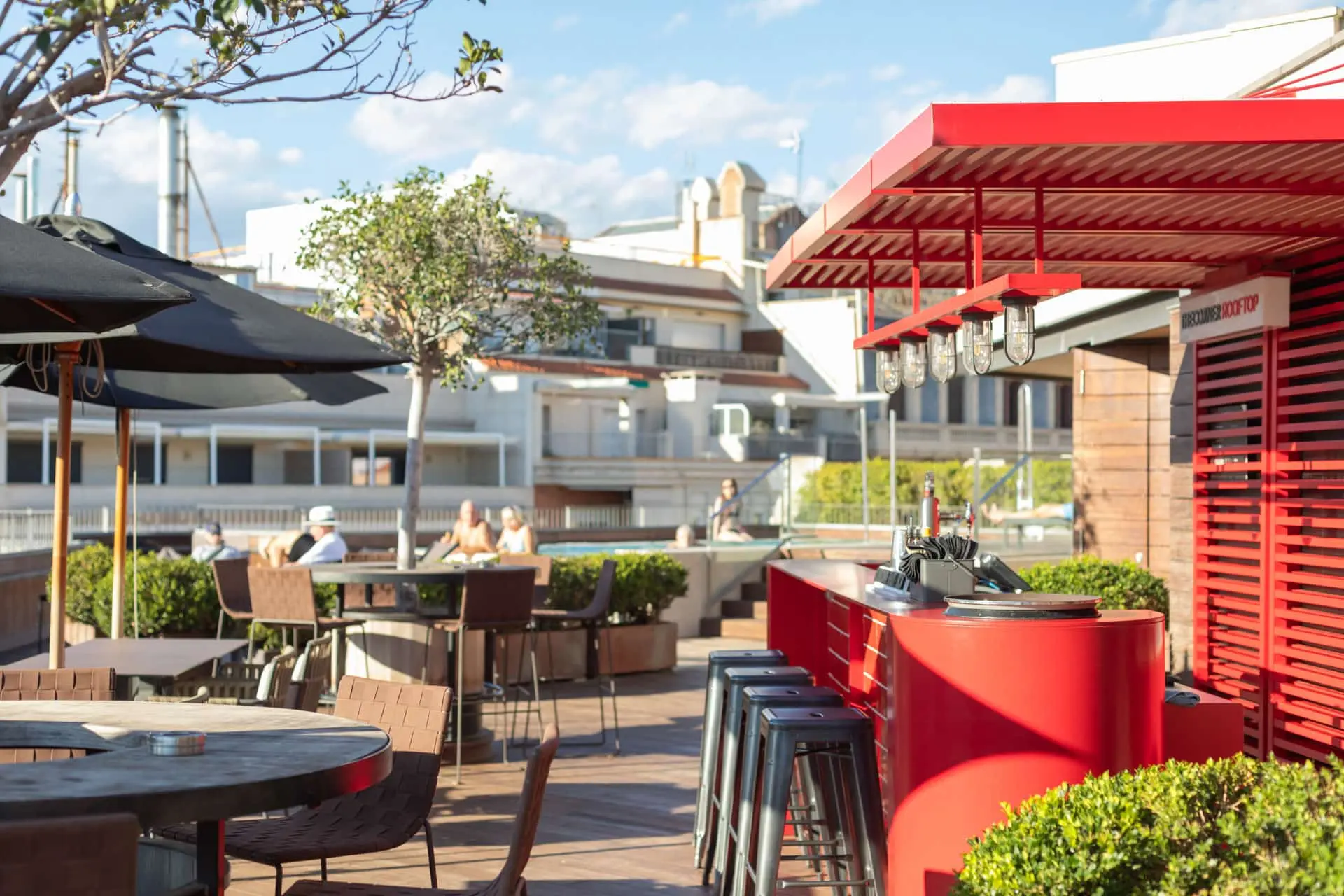 Terraza rooftop con mesas, sombrillas y bar junto a la piscina.