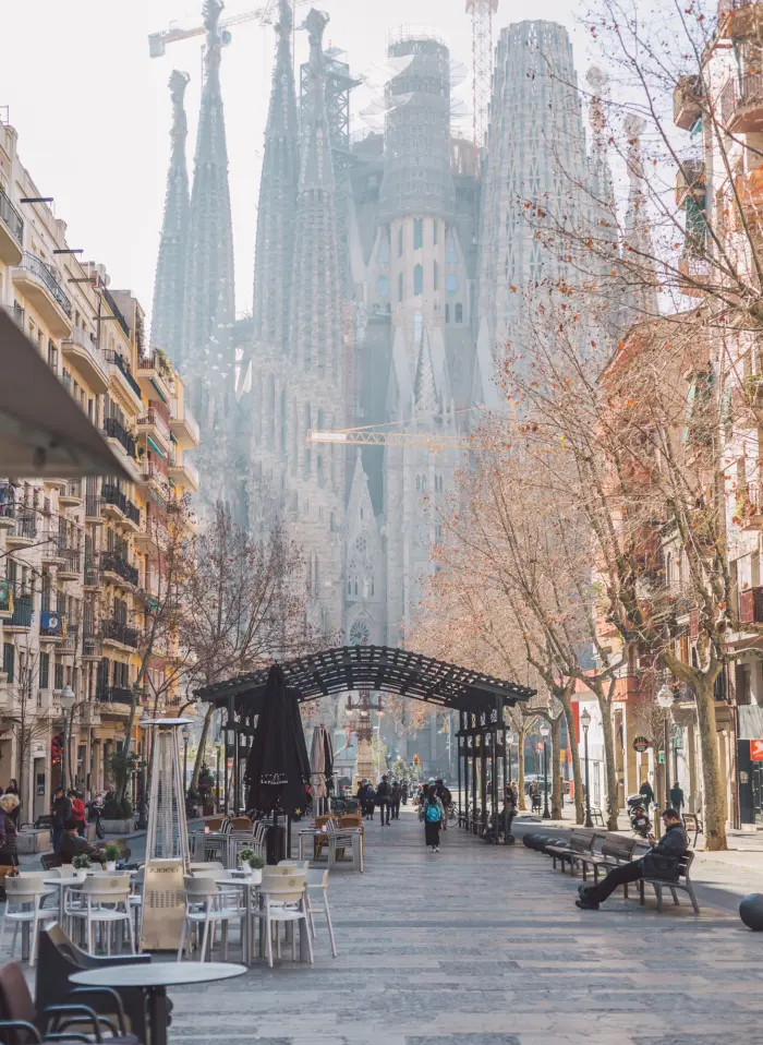 Calle peatonal con mesas al aire libre y una estructura de arco al fondo con edificios altos.