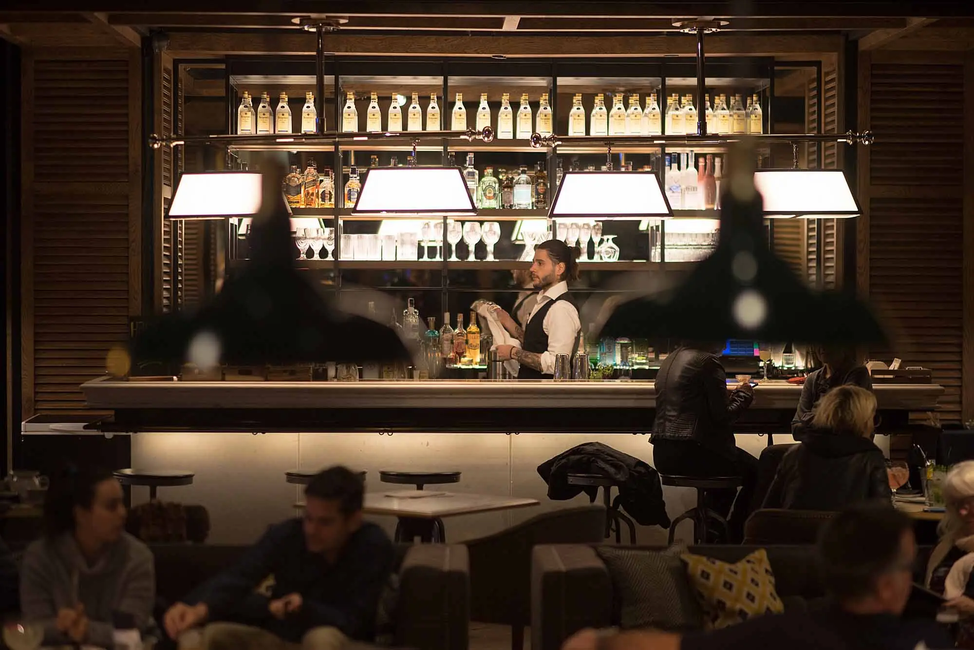 Bar con bancone e sgabelli accanto a scaffali pieni di bottiglie.