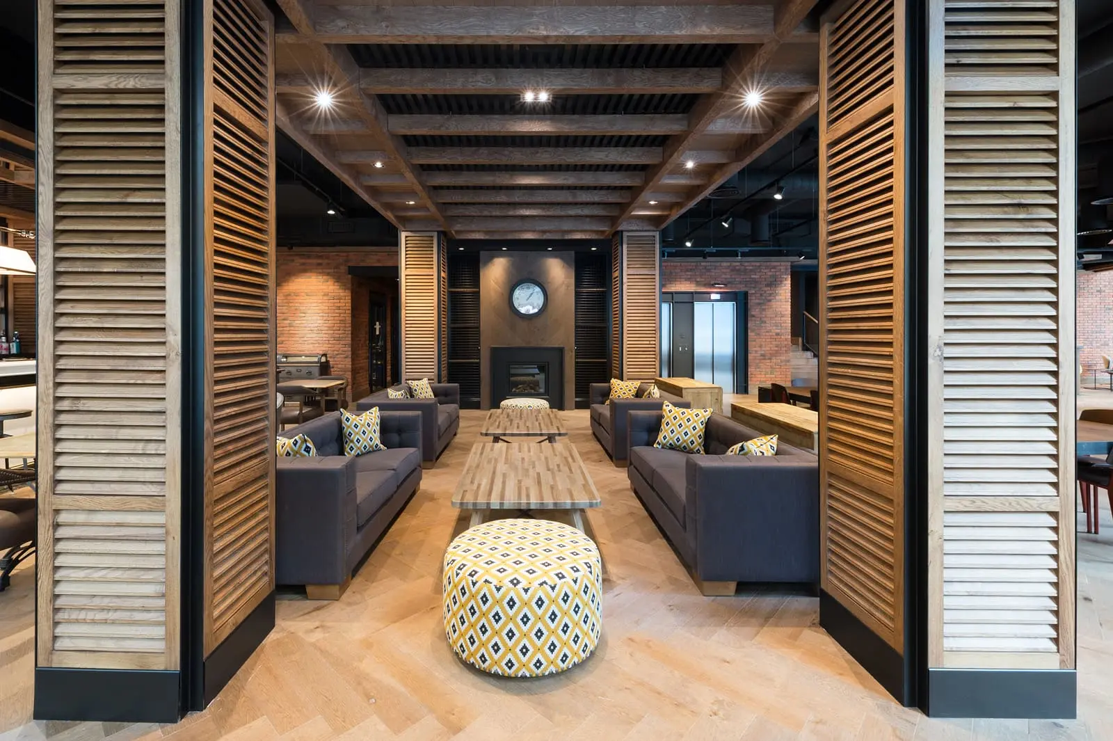 Un lobby moderno con sofás, mesas bajas y detalles de madera y ladrillo.