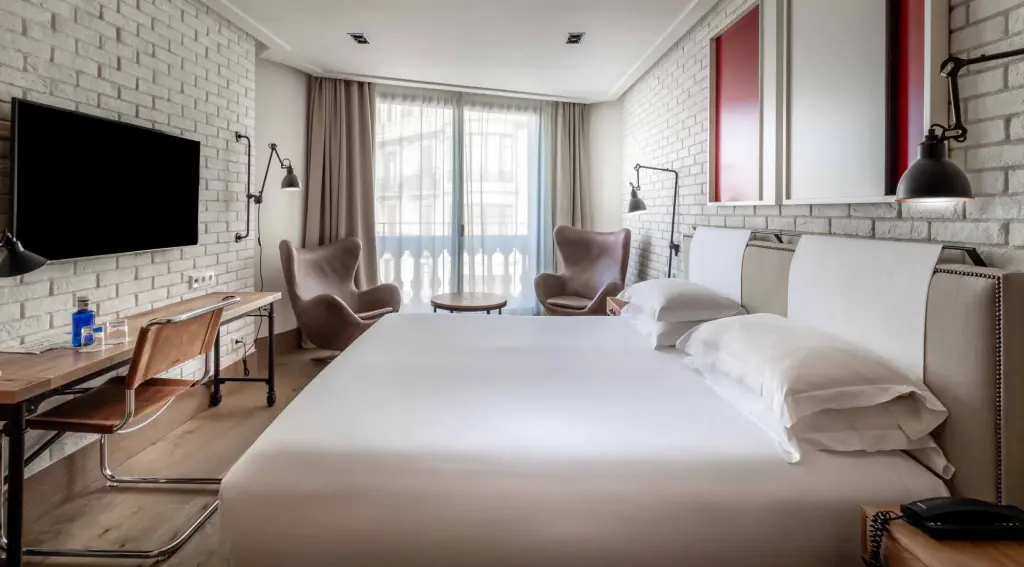 Dormitorio moderno con cama doble, televisor y ventana con cortinas en la pared del fondo.