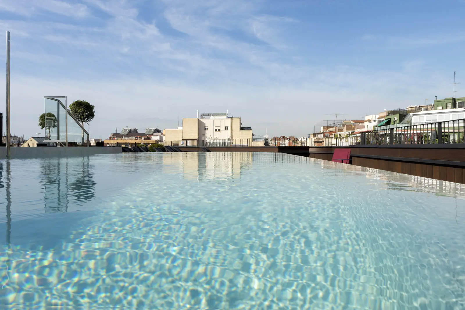 Se ve una piscina exterior con el borde de la terraza y edificios alrededor bajo un cielo despejado.