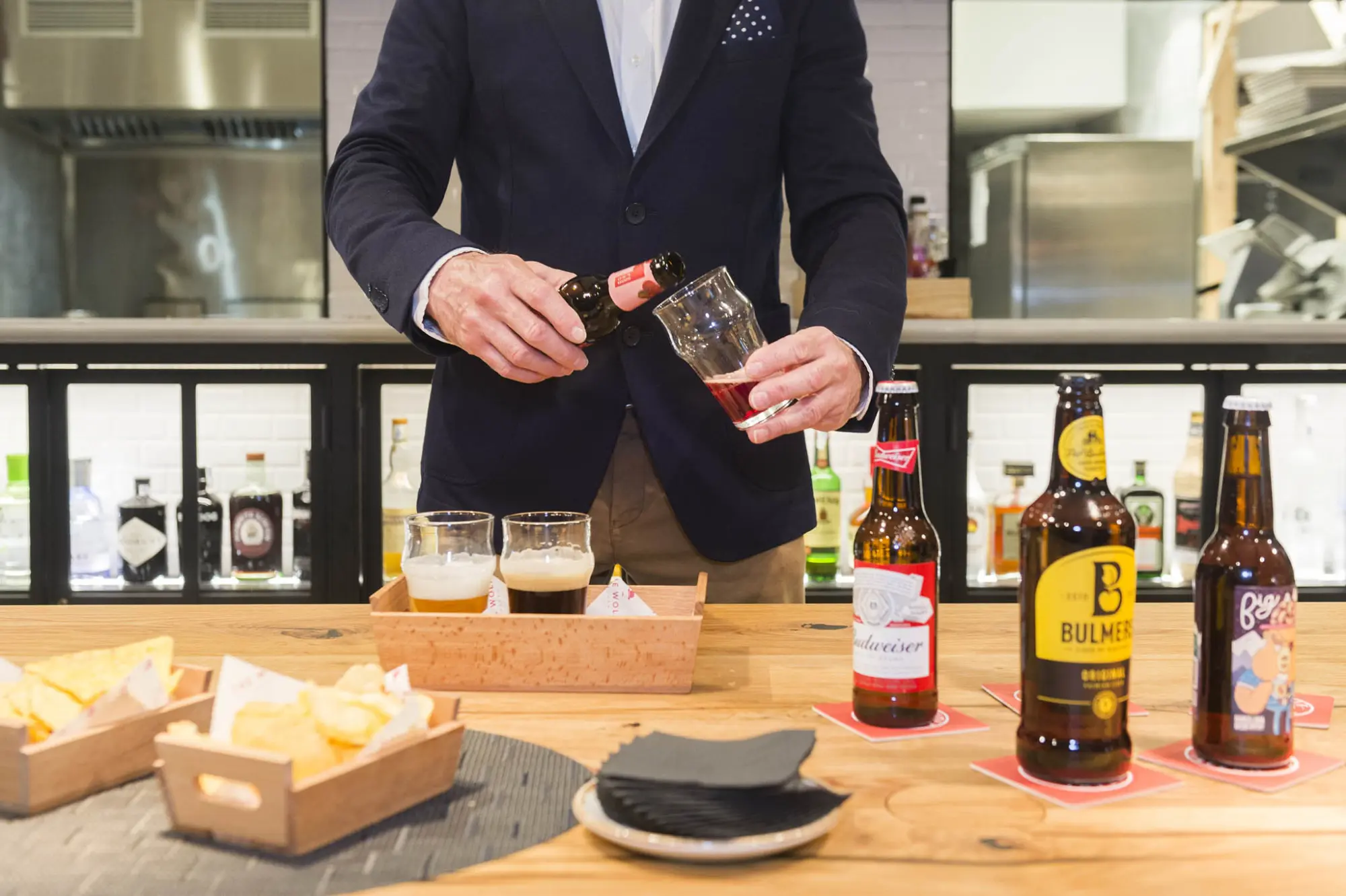 Un camarero sirve bebidas y hay botellas sobre una mesa en un bar interior.